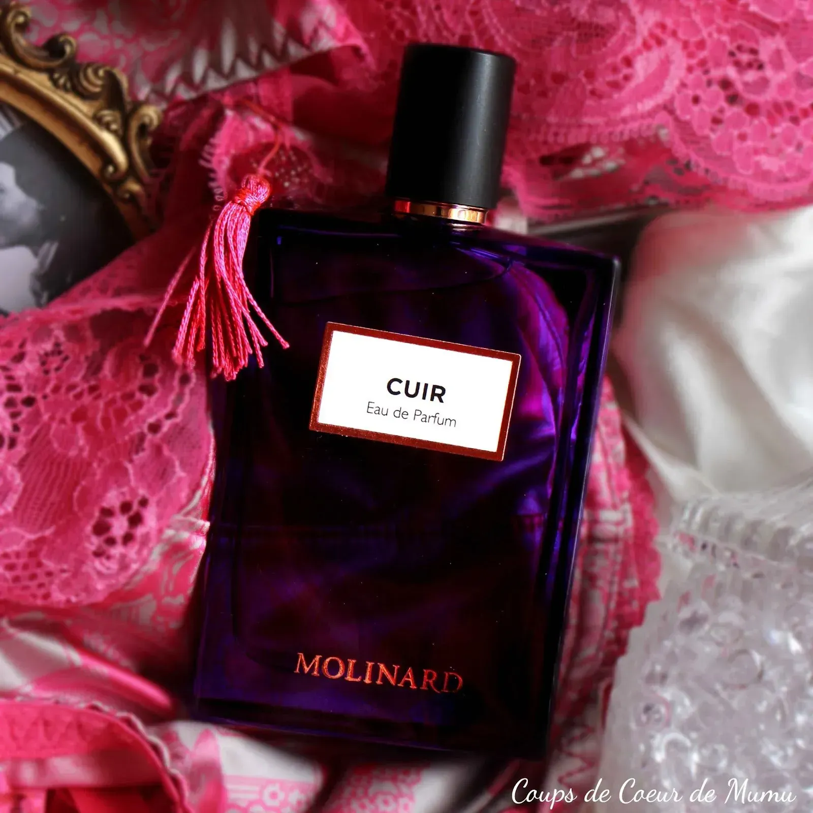 Flacone di profumo Molinard Cuir color porpora con tappo nero su tessuto di pizzo rosa.