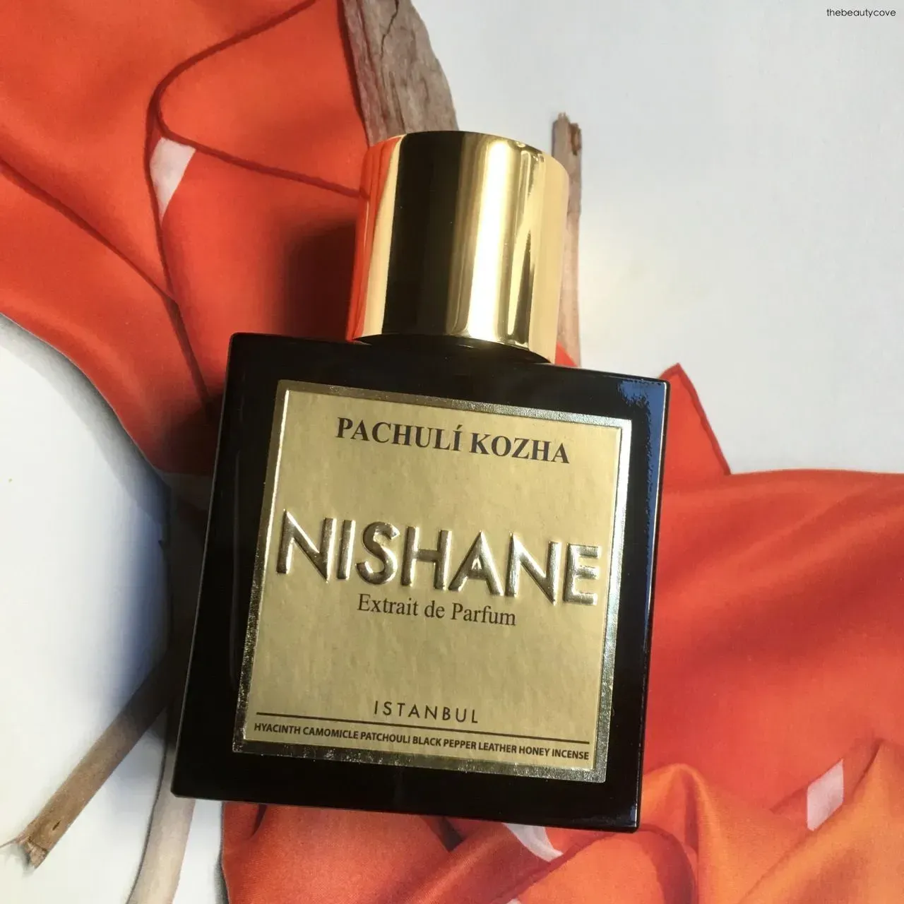 Flacone di profumo Nishane Pachuli Kozha con tappo dorato su sfondo di tessuto rosso.