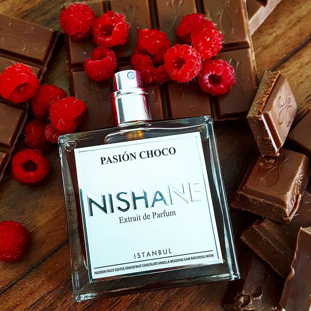 Flacone di profumo su tavolette di cioccolato con lamponi rossi e sfondo di legno.