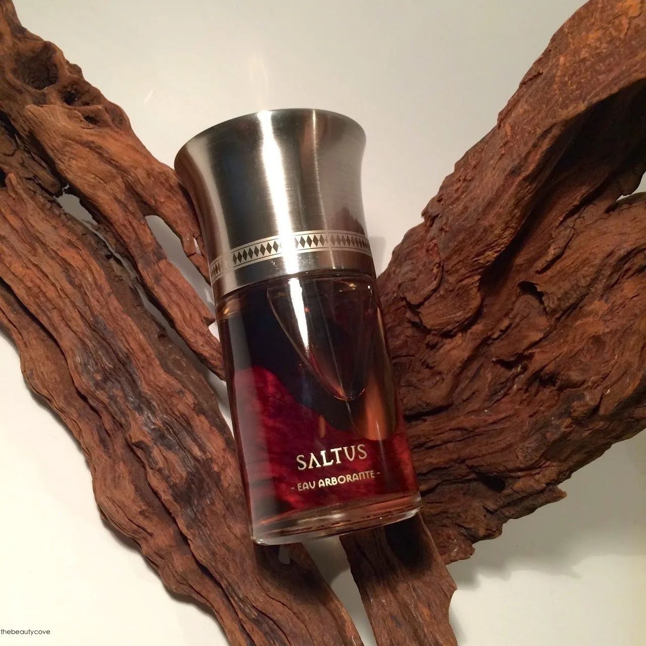 Flacone di profumo con tappo argentato su rami di legno rossastro, con etichetta SALTUS.