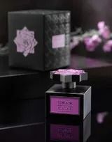 Flacone di profumo nero con etichetta e tappo rosa, posizionato accanto a una scatola regalo nera coordinata