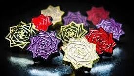 Rose di carta colorate nei toni del rosso, viola, crema e verde, disposte su uno sfondo scuro.