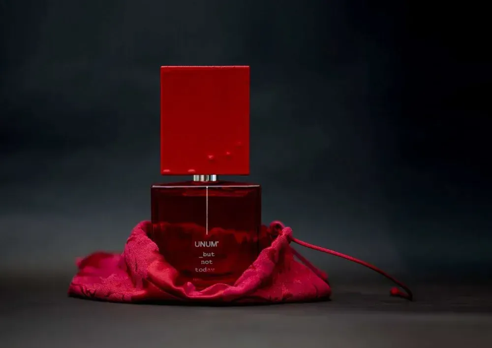 Flacone di profumo rosso su tessuto rosso contro sfondo scuro.