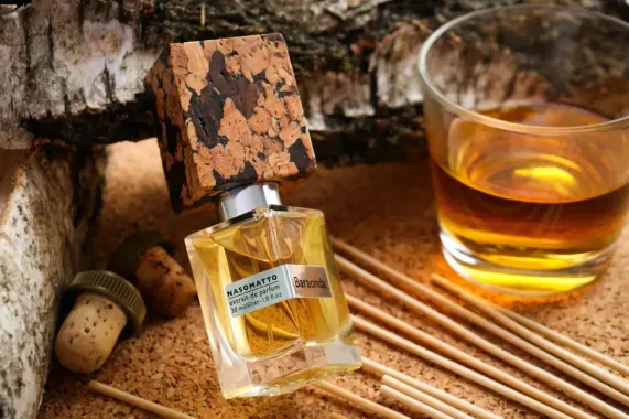 Una boccetta di profumo accanto a un bicchiere da whisky, tappi di sughero e bastoncini di bambù