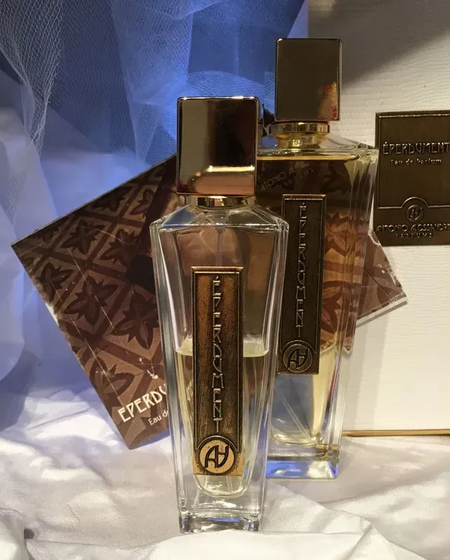 Due flaconi di profumo trasparenti con tappo dorato su una superficie riflettente, con una scatola decorata sullo sfondo.