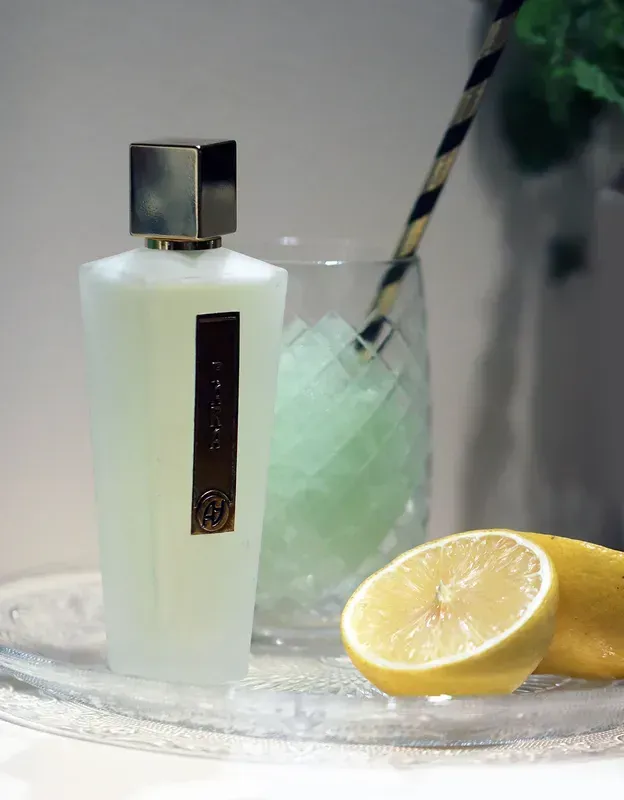 Una boccetta di profumo accanto a una bevanda al lime e fette di limone su un vassoio.
