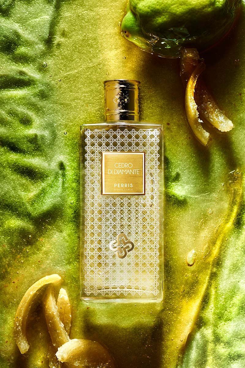 Flacone di profumo dorato su tessuto verde testurizzato con dettagli dorati metallici.