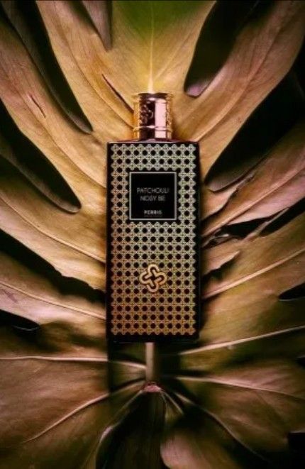 Flacone di profumo con etichetta nera e motivo a pois dorati su uno sfondo a forma di foglia.