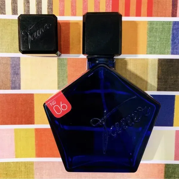 Flacone di profumo pentagonale blu con tappo nero su sfondo a righe colorate.