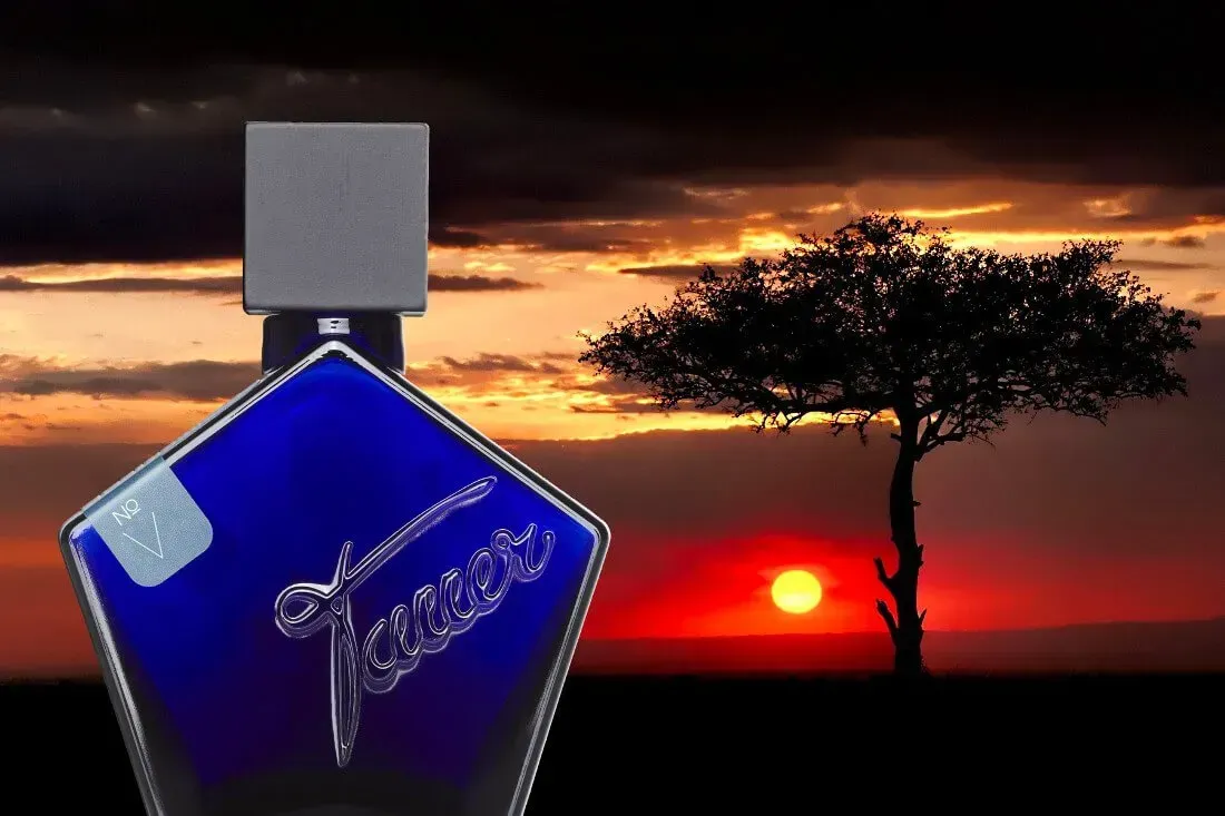 Flacone di profumo blu con tappo argentato sullo sfondo di un cielo al tramonto e di un albero in controluce.