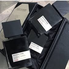 Scatole e flaconi di profumo di lusso neri, disposti su un tessuto di raso nero con un cartoncino beige sullo sfondo.