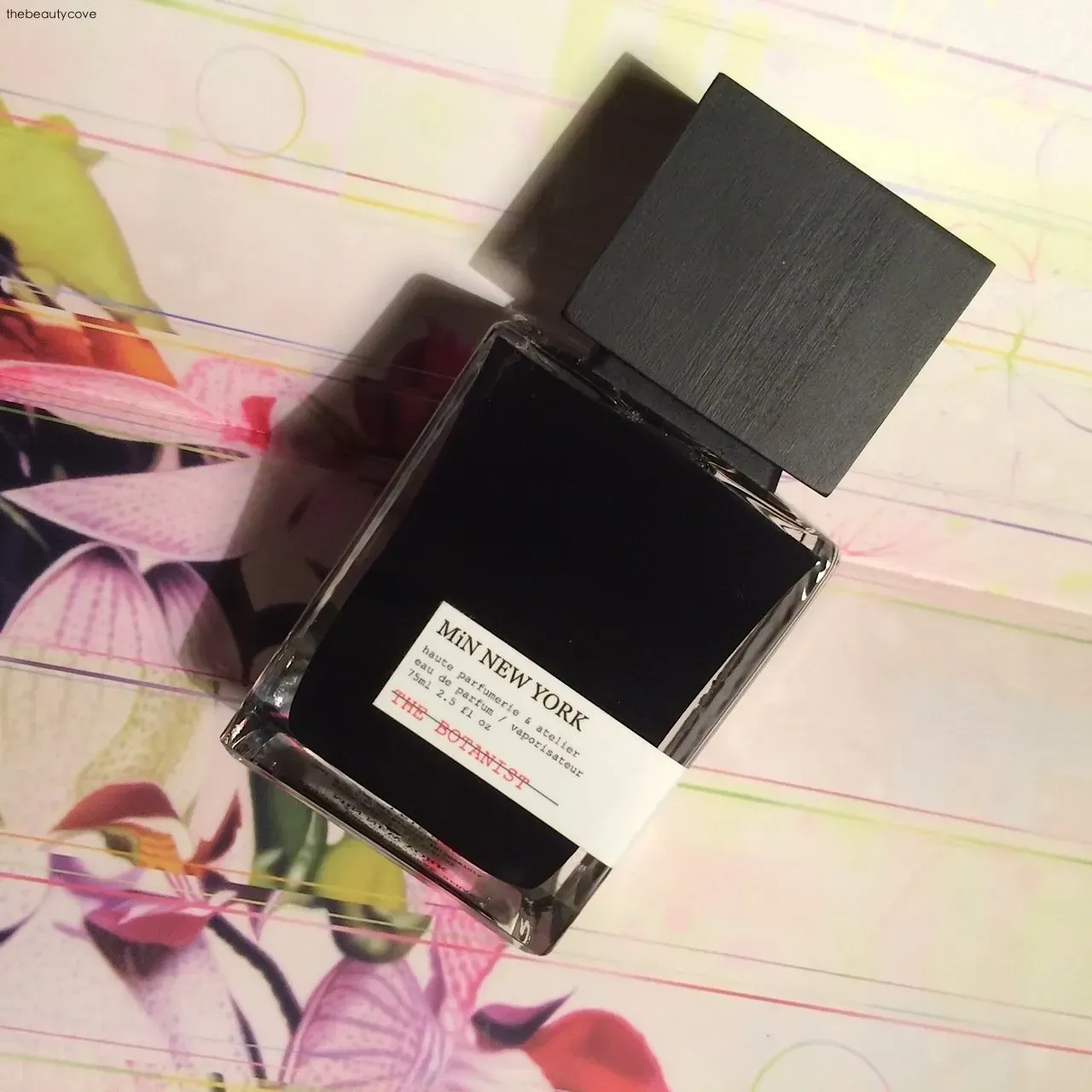 Flacone di profumo nero con tappo quadrato su sfondo floreale da quaderno