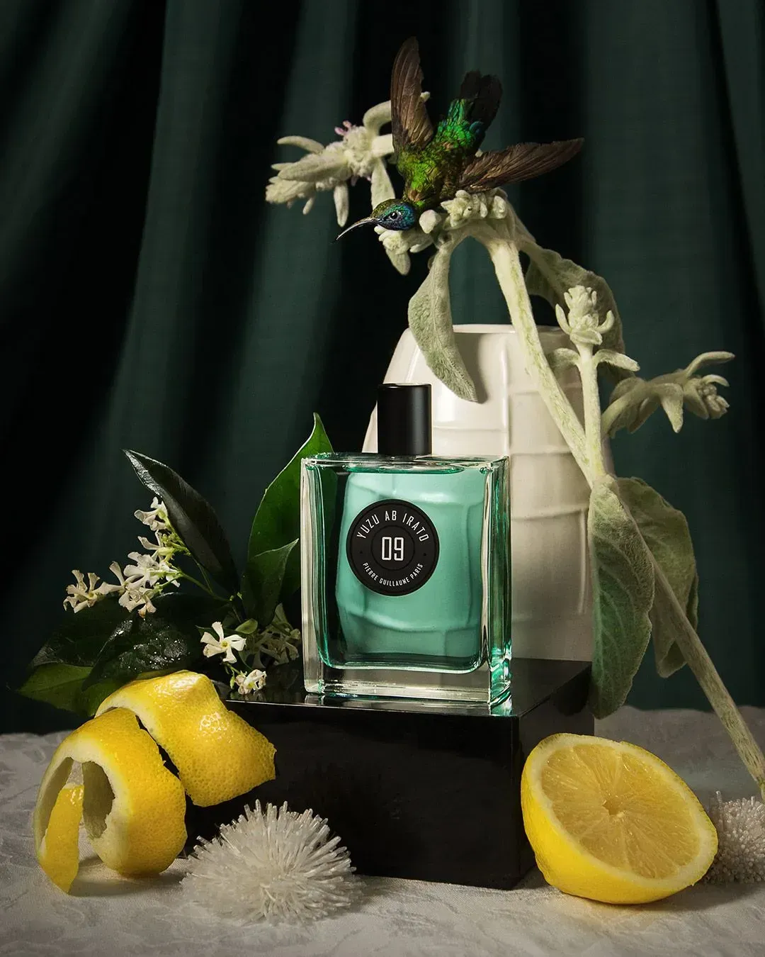 Flacone di profumo verde con fiori bianchi e fette di limone su sfondo scuro