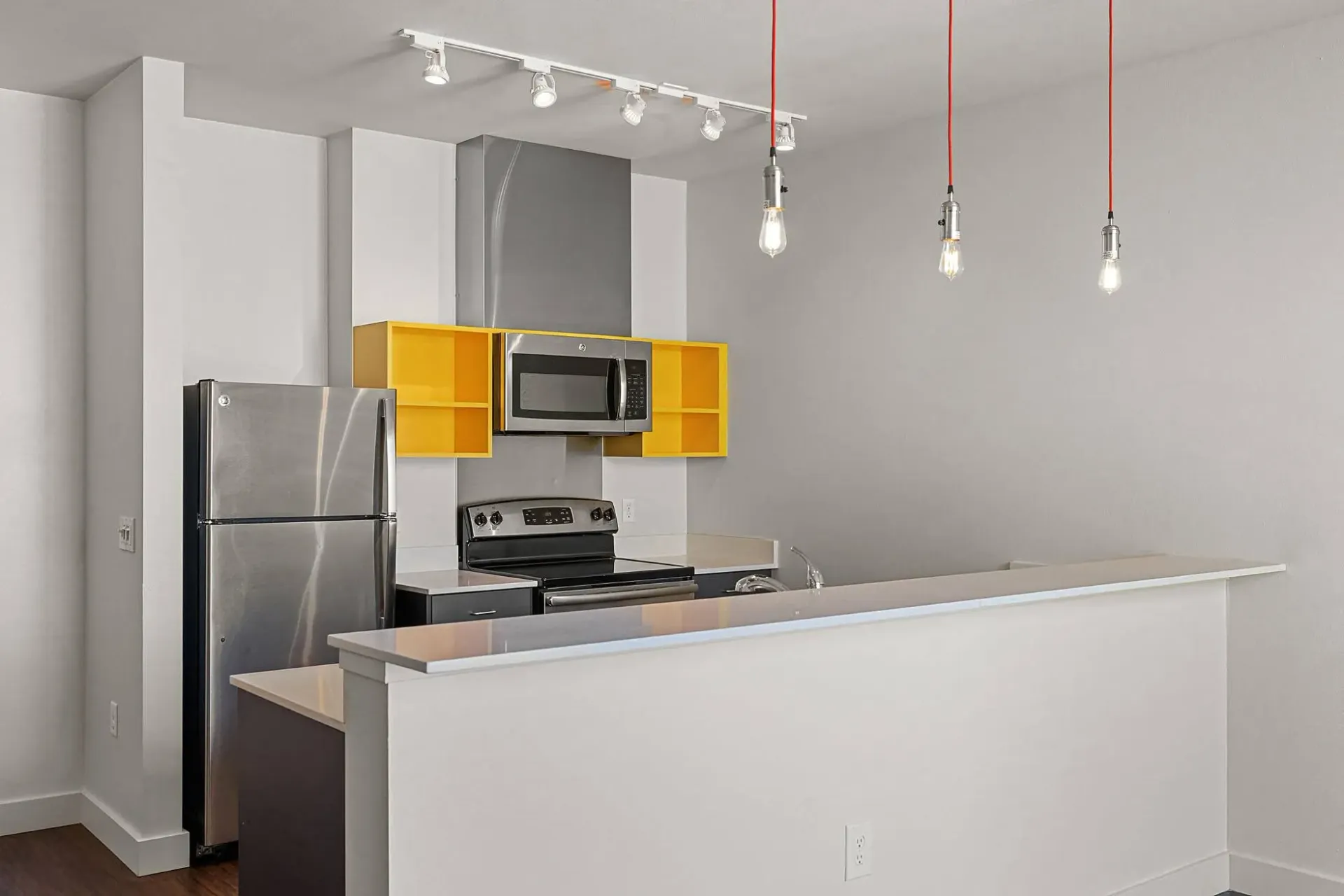 Modern kitchen with stainless steel appliances, yellow accent shelves, and pendant lighting.