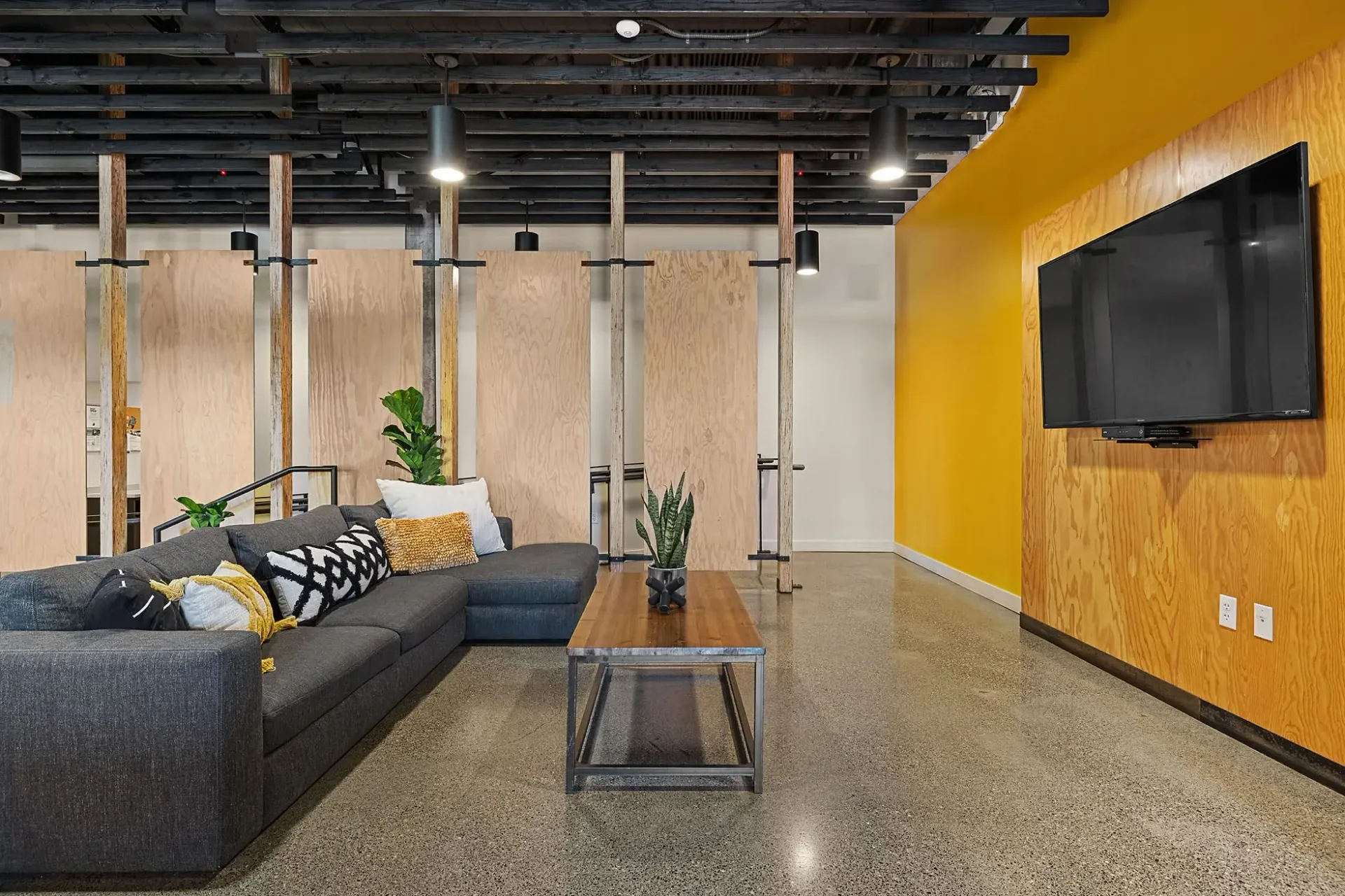 Modern communal lounge area with a large sectional sofa, coffee table, and mounted TV.
