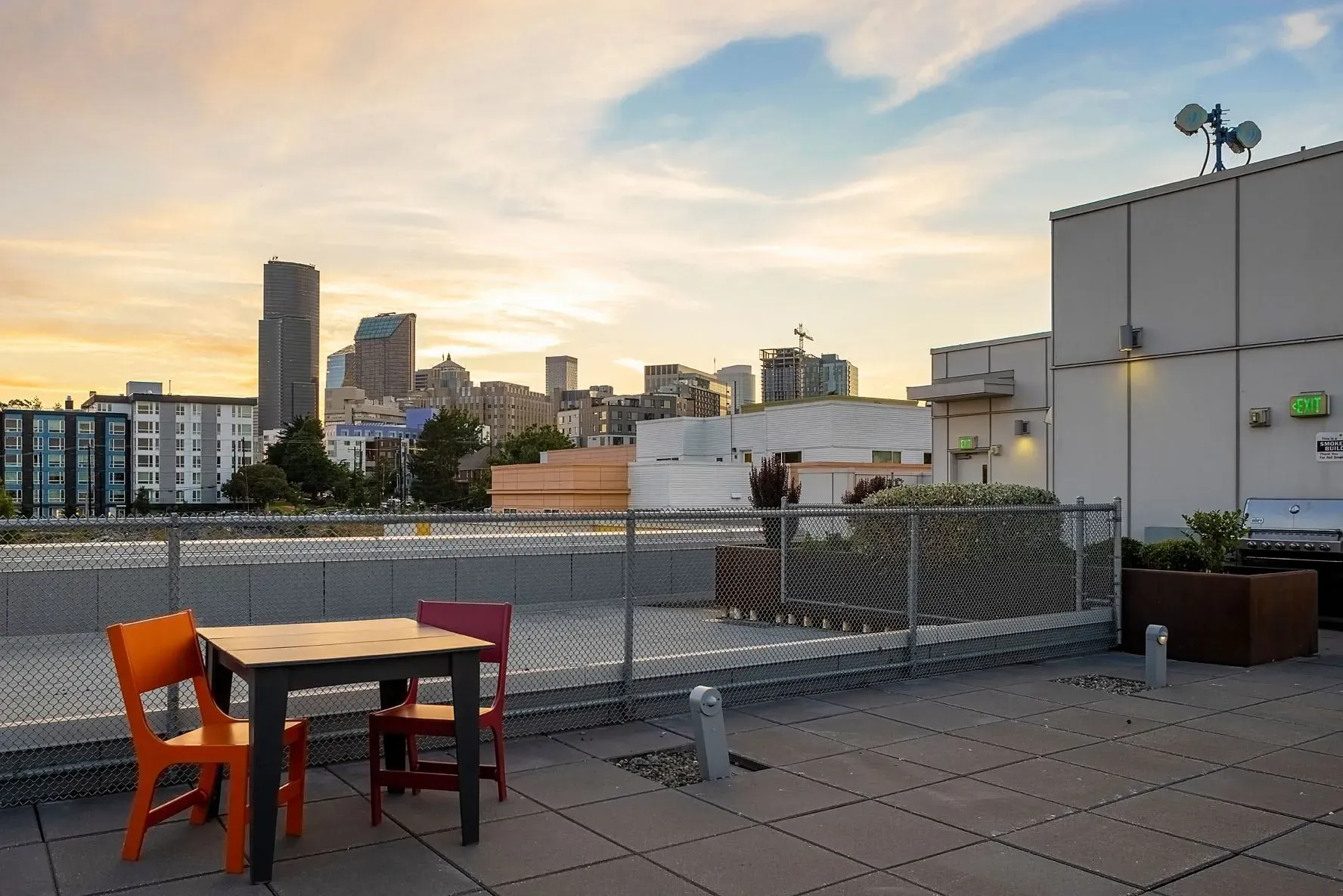 Rooftop patio with city skyline view, table and chairs, and grill.
