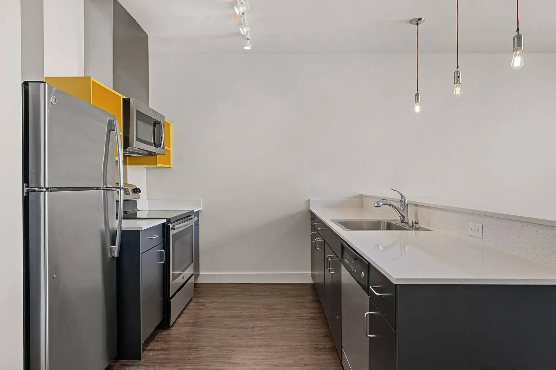 Modern apartment kitchen with stainless steel appliances, dark cabinets, and white countertops.