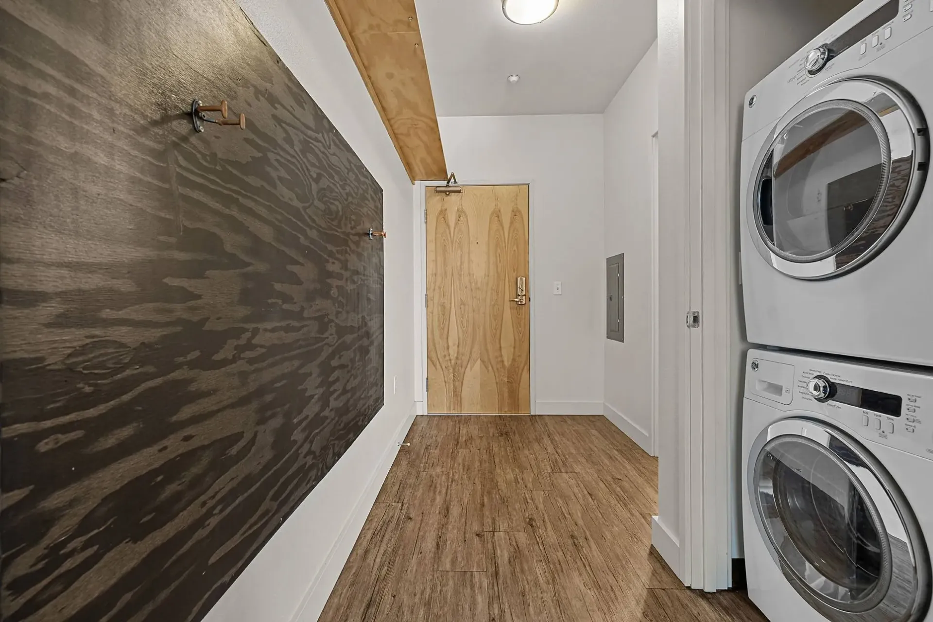 Apartment entryway with stacked washer and dryer and decorative wall panel.