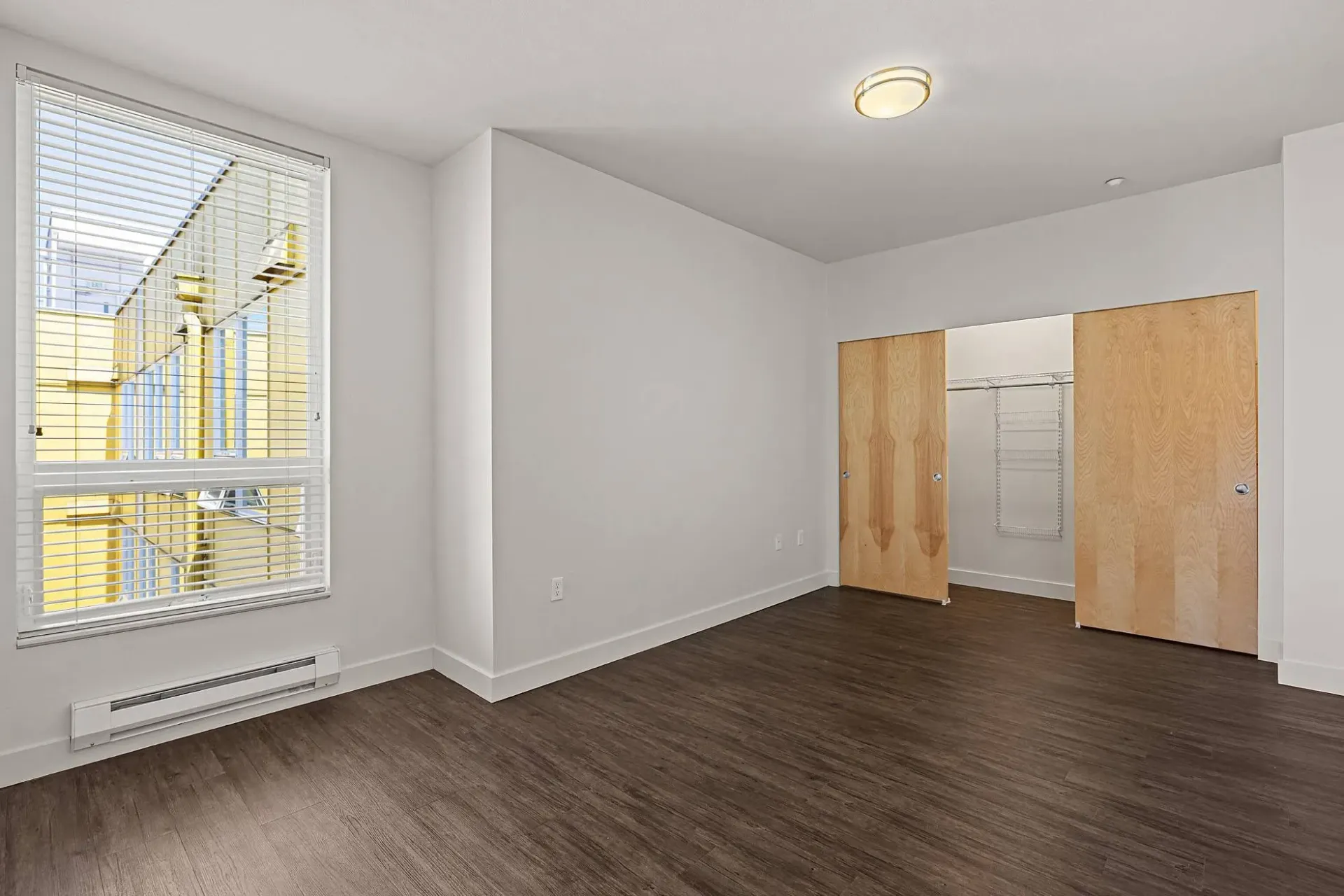 Empty bedroom with large window and closet doors.