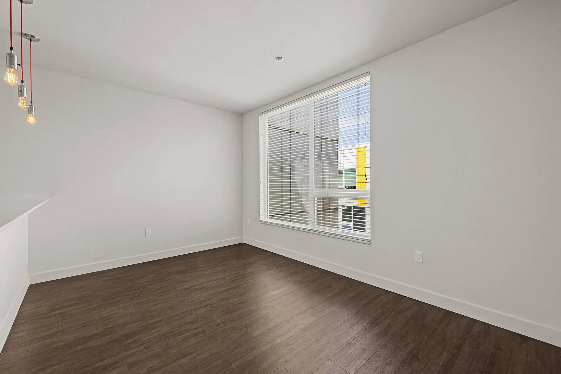 Interior view of an empty apartment living space with dark wood floors and a large window.