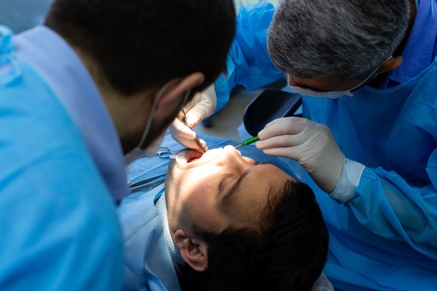 Dentists in blue scrubs treating a patient with bright light during a dental procedure