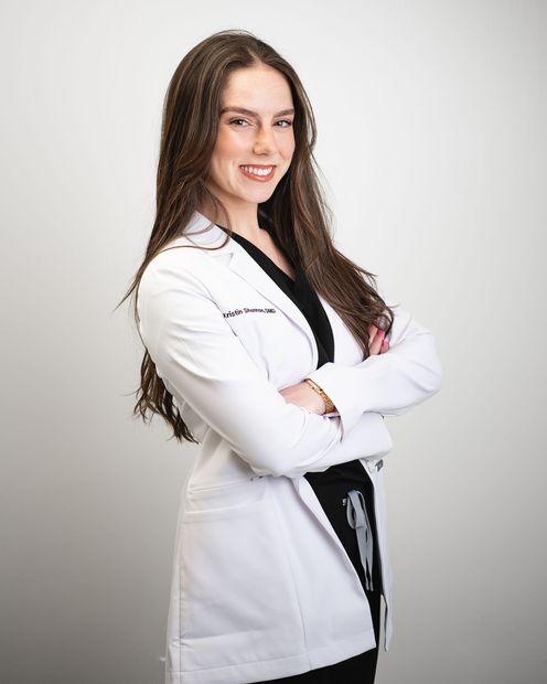 Smiling doctor in a white coat standing in a bright office with a landscape painting behind her