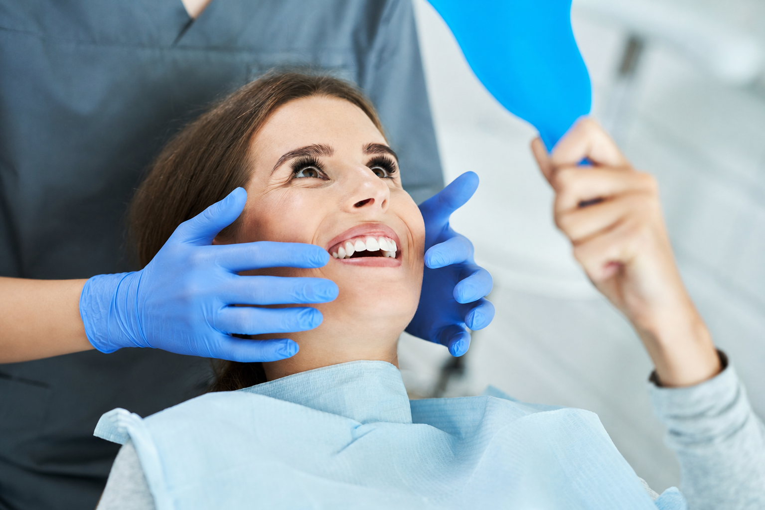 Dentist examining a smiling patient in a dental chair with blue gloves and dental tools