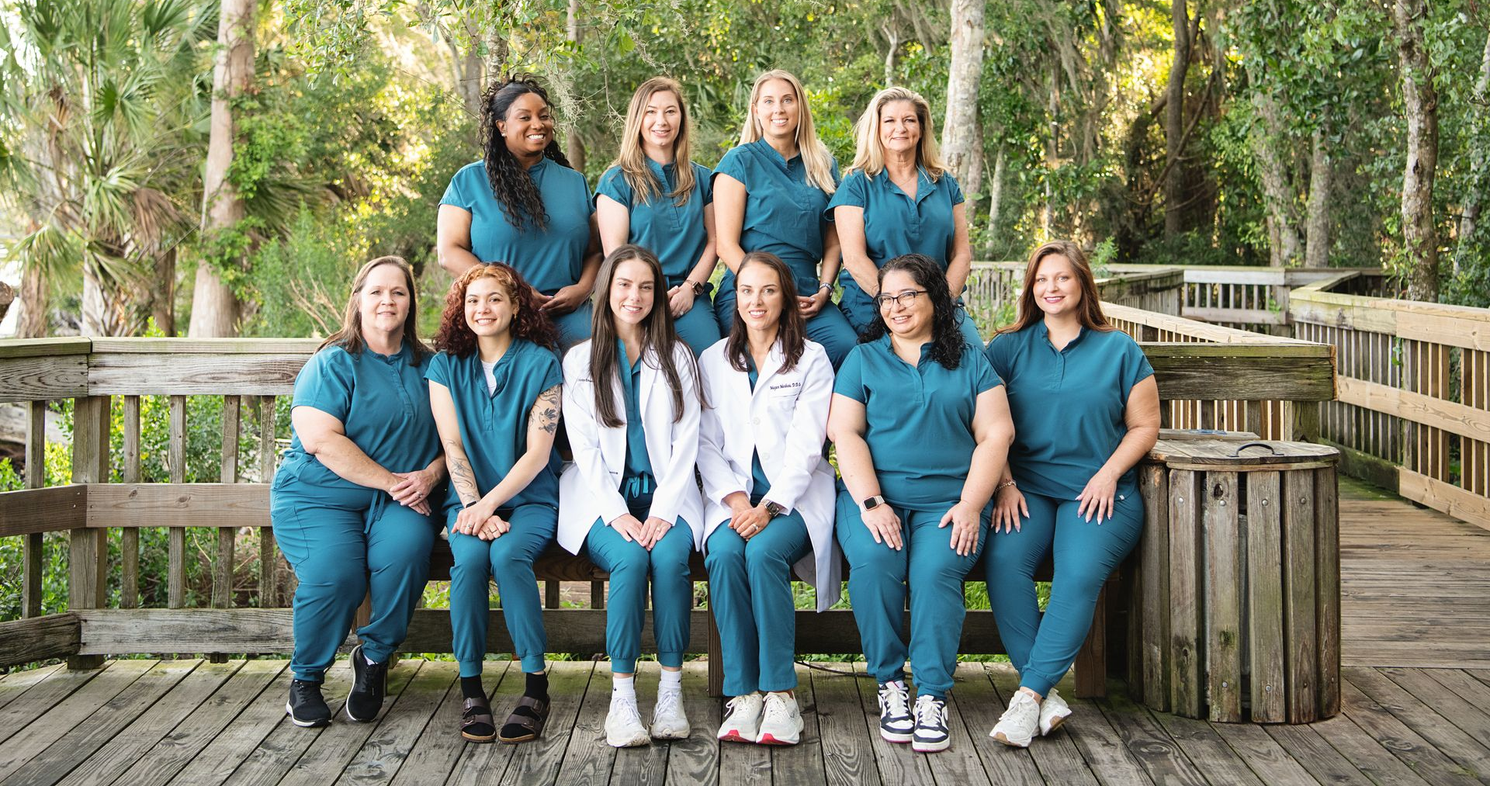 Group of nurses in teal scrubs posing together on a wooden deck outdoors.