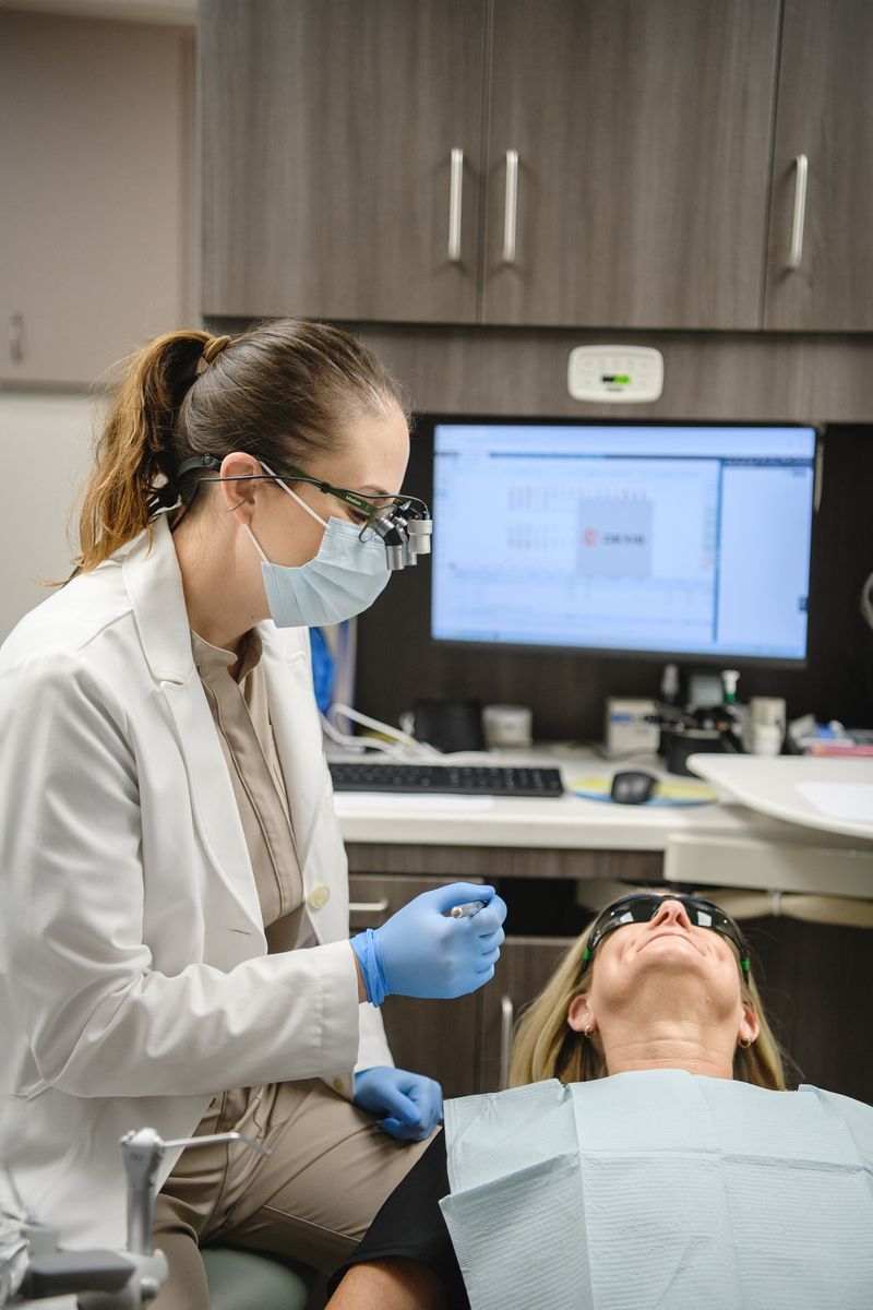 Dentist examining patient in a clinic, wearing mask and gloves beside a dental chair and monitor