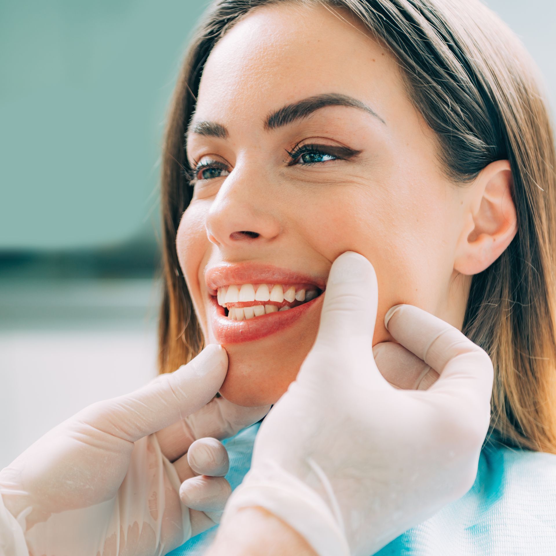 Dentist examining a smiling patient’s teeth with gloved hands