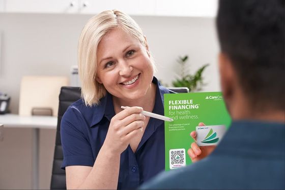 Woman in navy shirt presenting a green brochure with a pen in an office setting