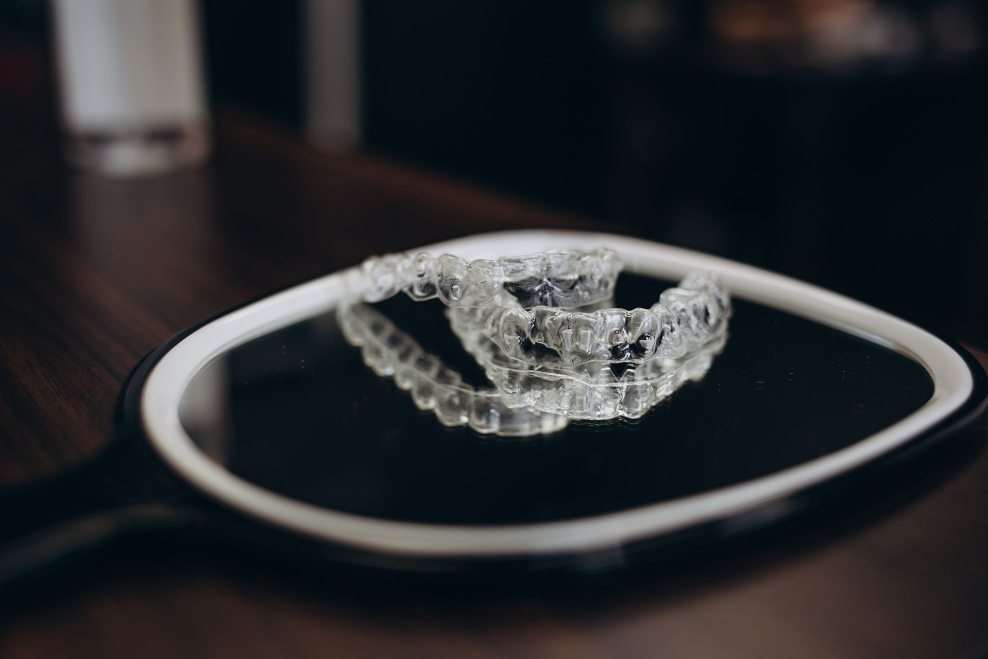 Clear dental aligner on a white-rimmed black plate on a dark table