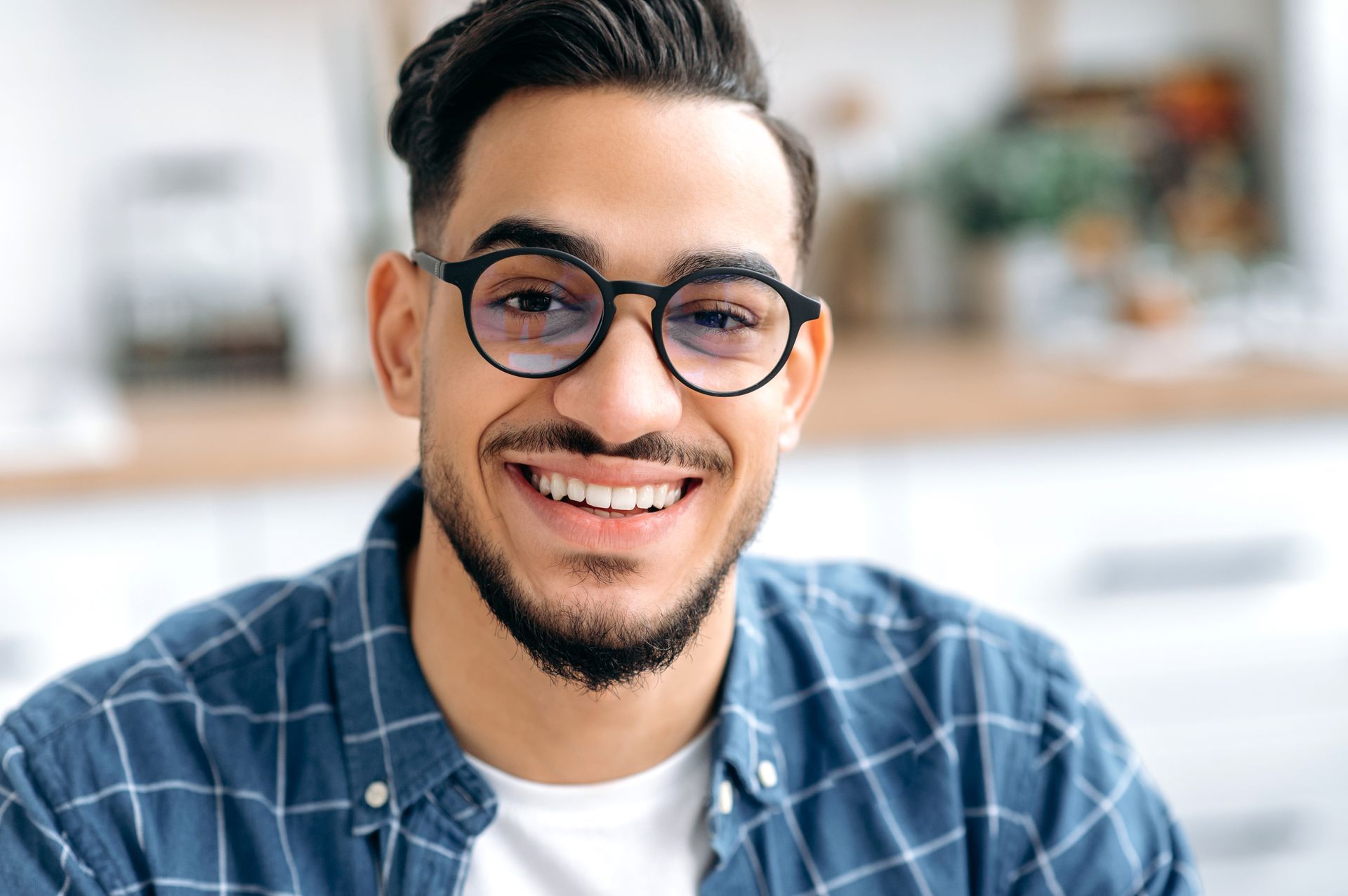 Smiling man with glasses and blue plaid shirt in a bright indoor setting