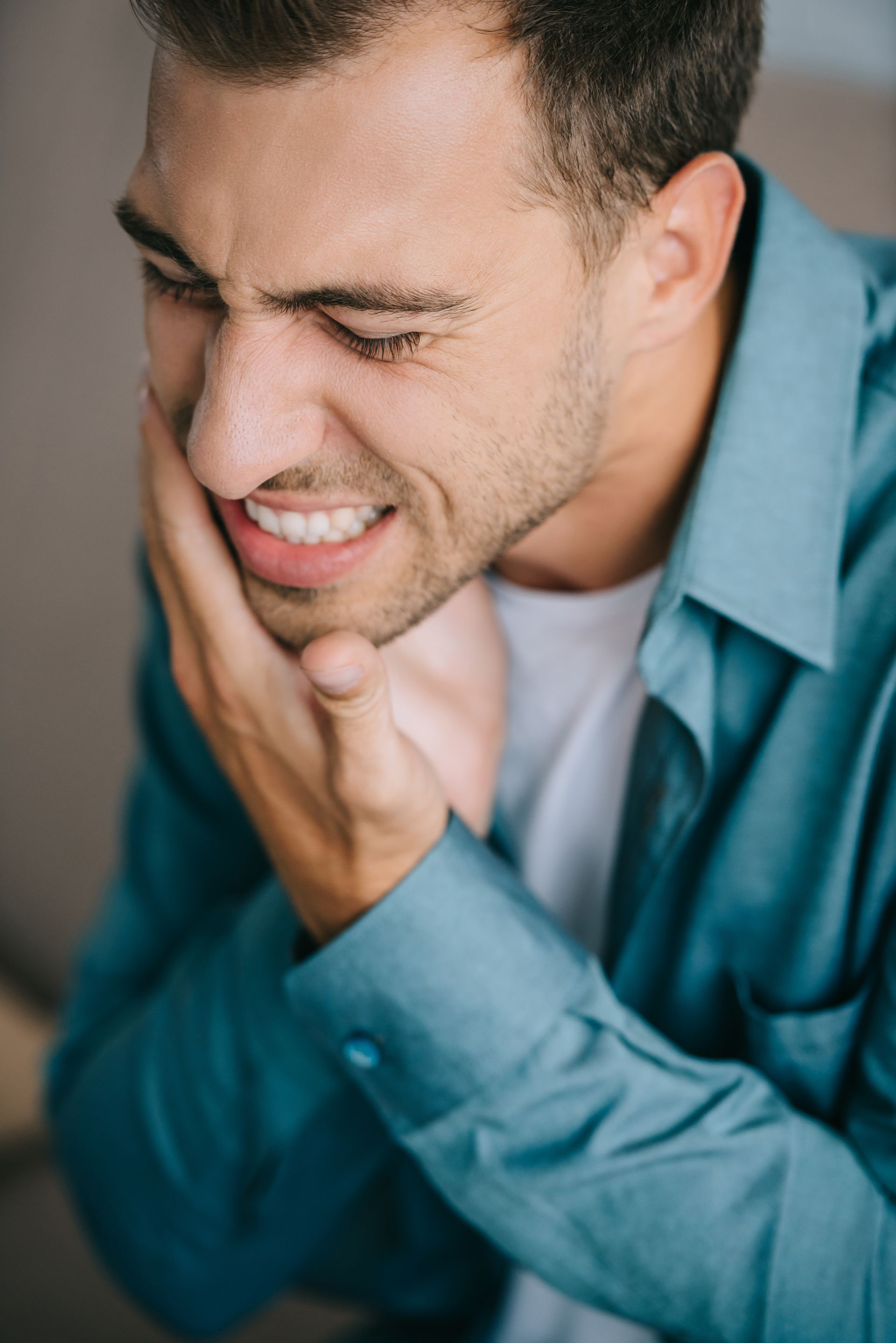 Man in a teal shirt holding his jaw, wincing in pain or discomfort