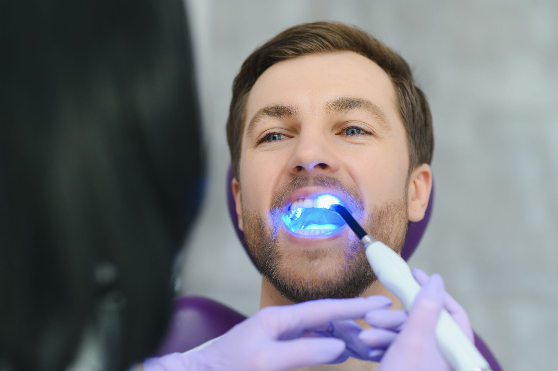Dentist using a blue light dental tool on a patient wearing a cheek retractor