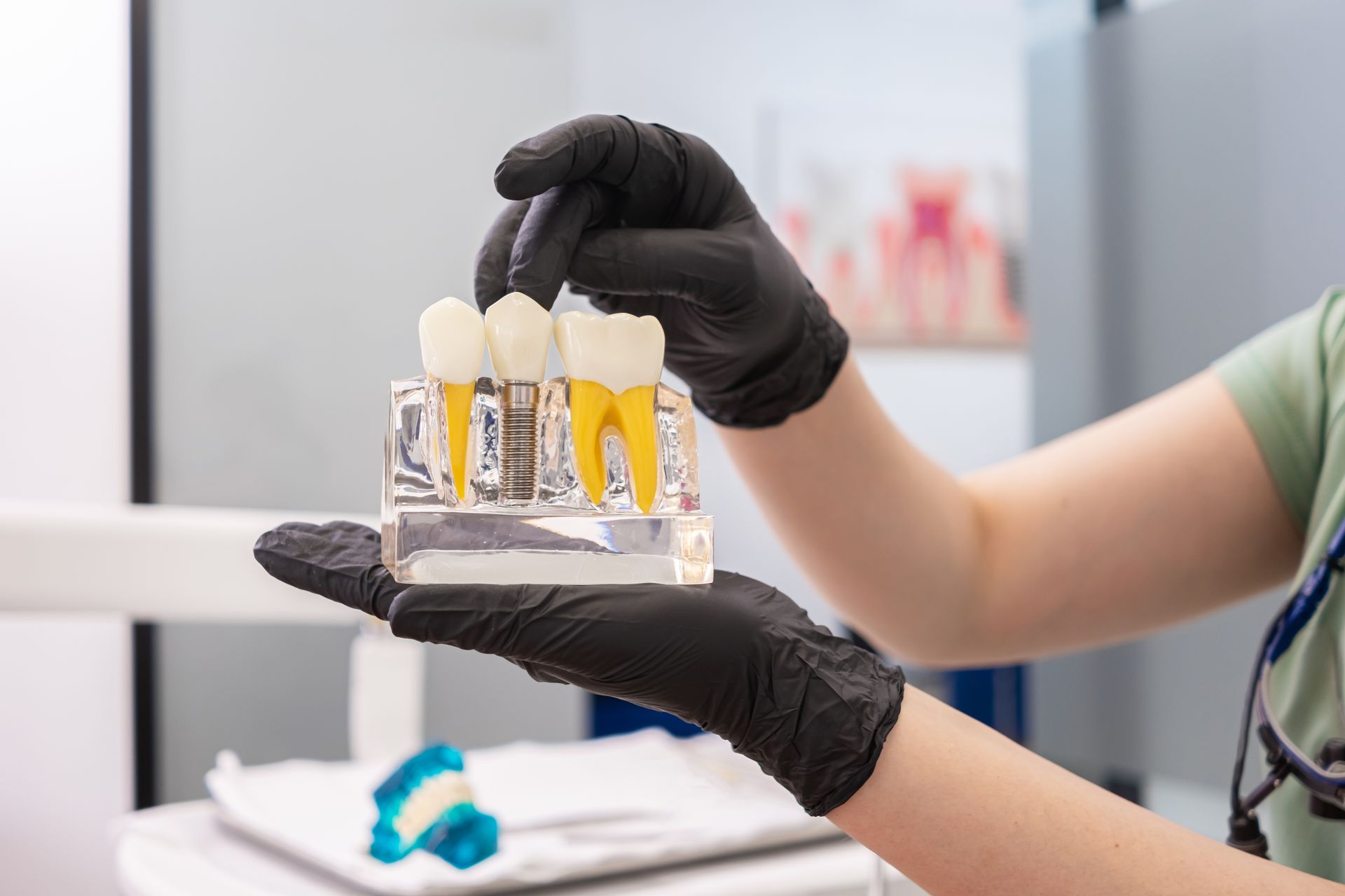 Gloved hands holding two dental crowns over a table in a dental clinic