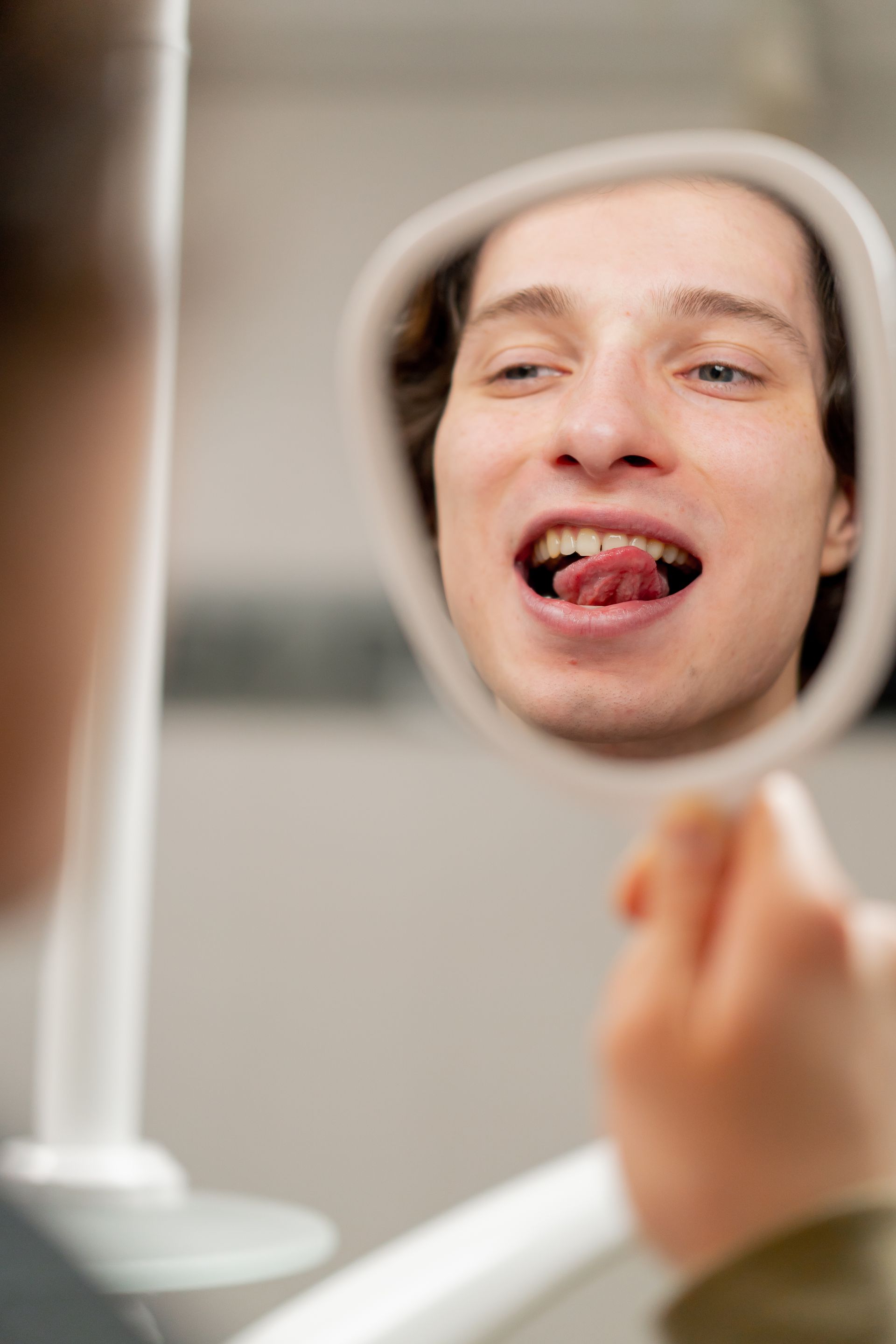 Person examining their teeth in a handheld mirror, with a tooth missing.