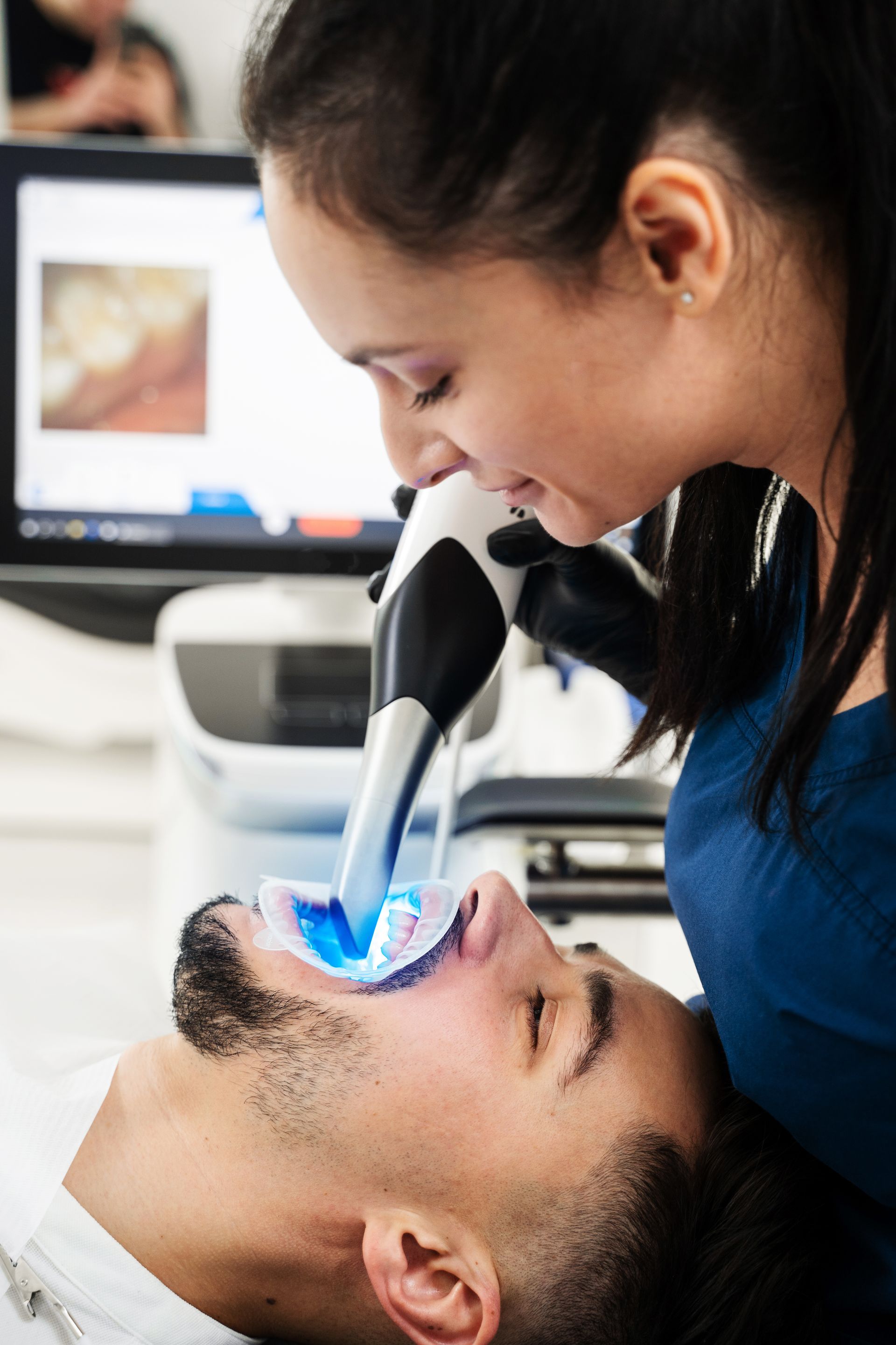 Dentist using a blue-lit dental tool on a patient reclined in a clinic chair