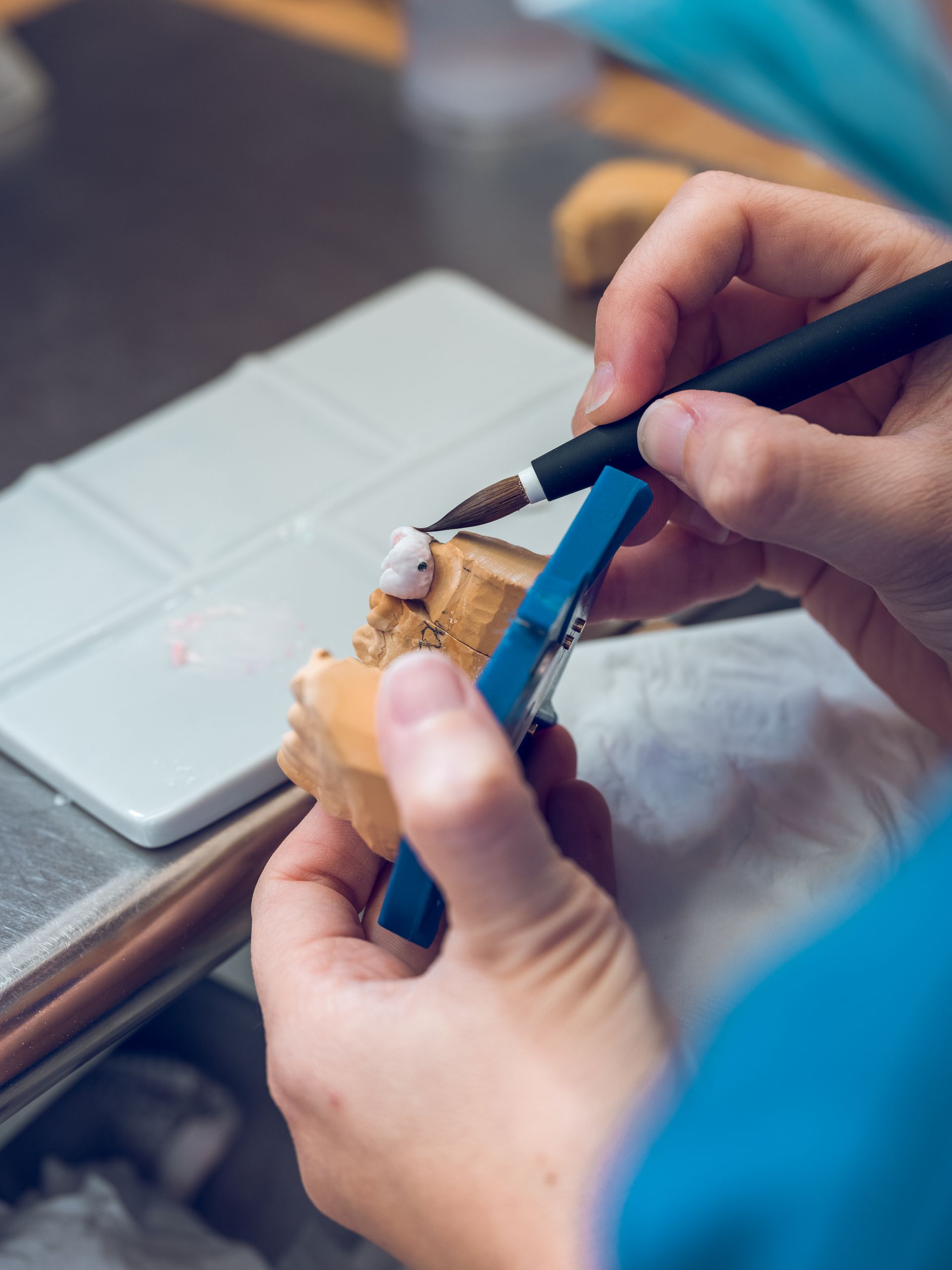 Hands using a small brush to apply icing on a pastry beside a laptop.