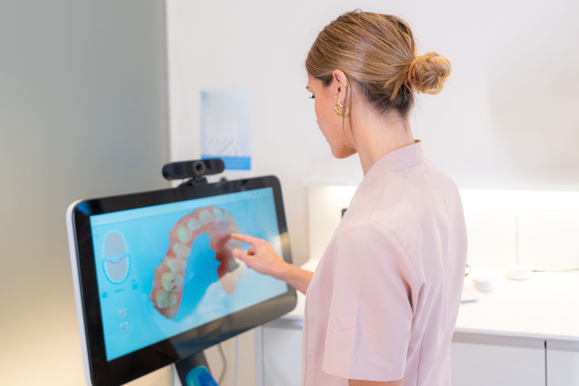 Person touching a 3D dental scan on a touchscreen in a bright clinic