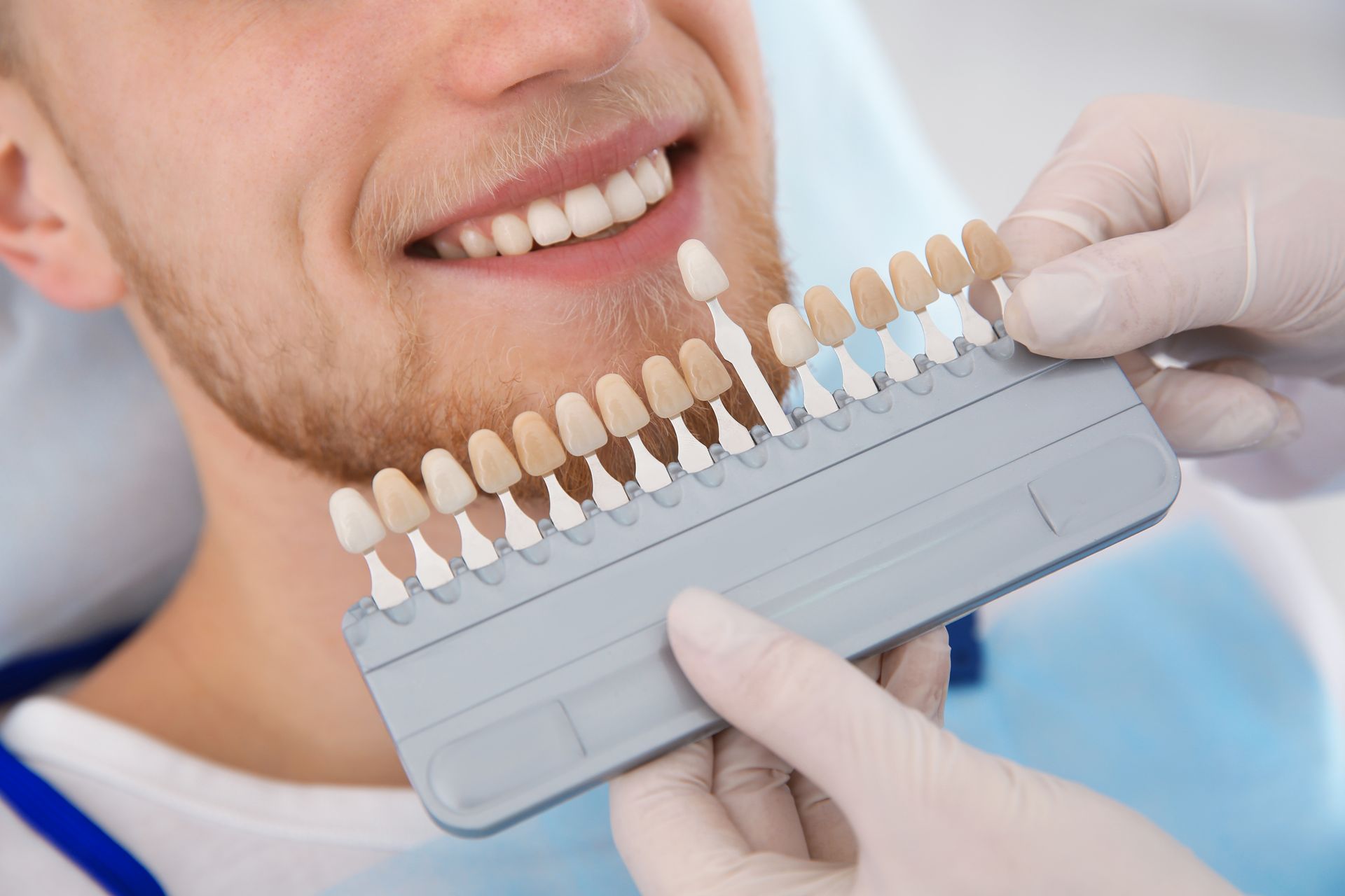 Dentist holding a shade guide to a smiling patient’s teeth during a dental consultation