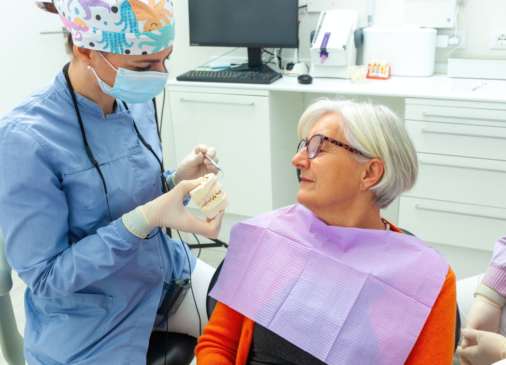 Dentist examining a smiling patient in a dental clinic, wearing a purple bib and mask