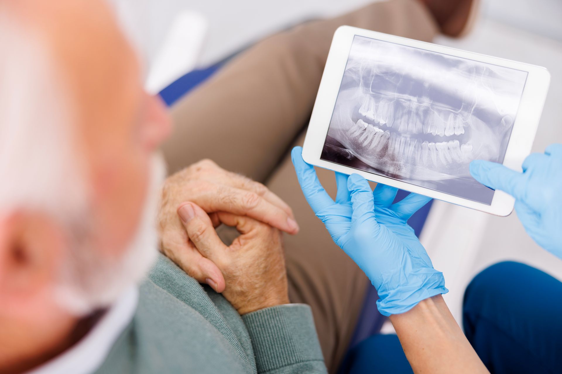 Dentist showing a patient a dental X-ray while wearing blue gloves and holding their hand