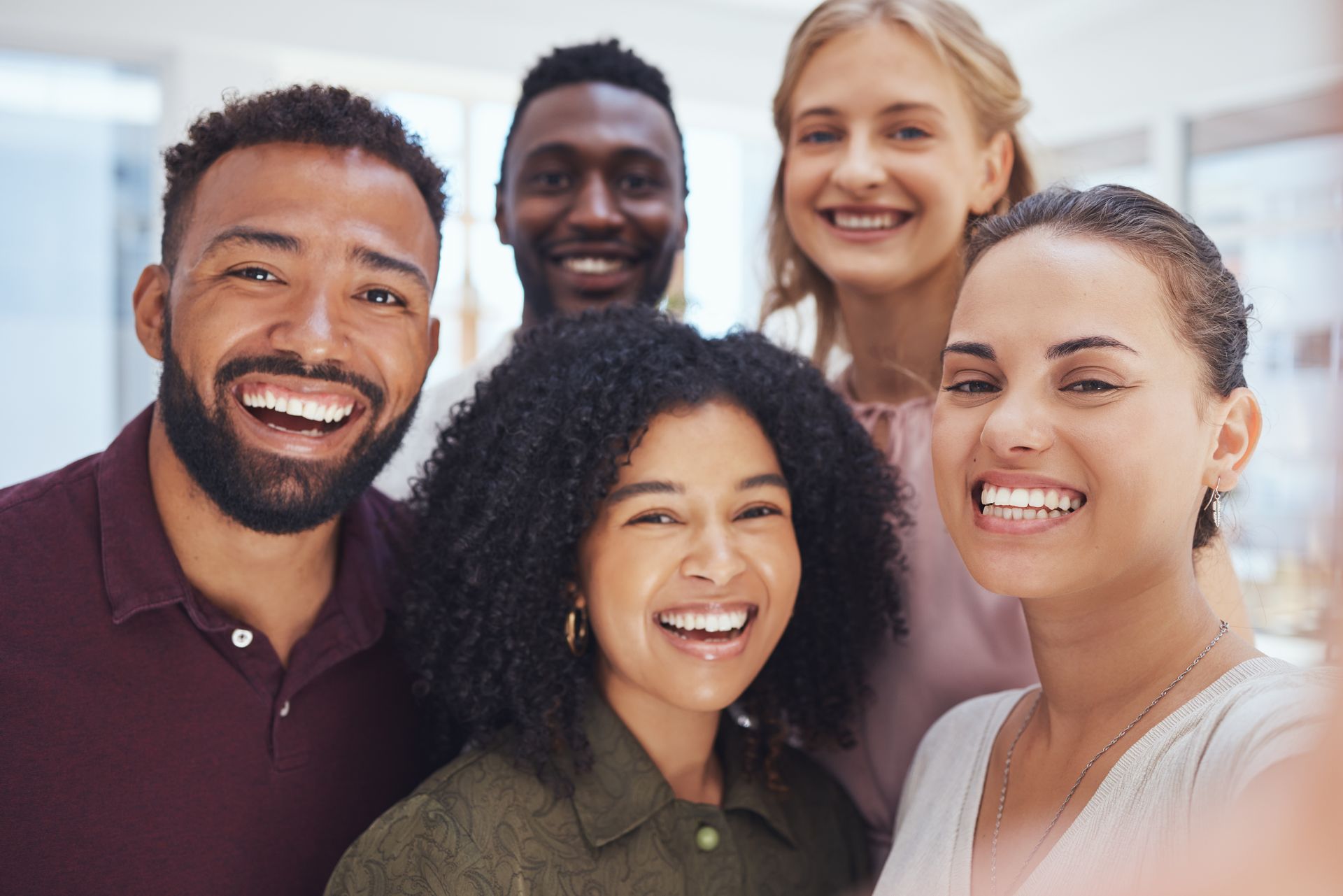 Five smiling people posing closely together outdoors against a bright sky.