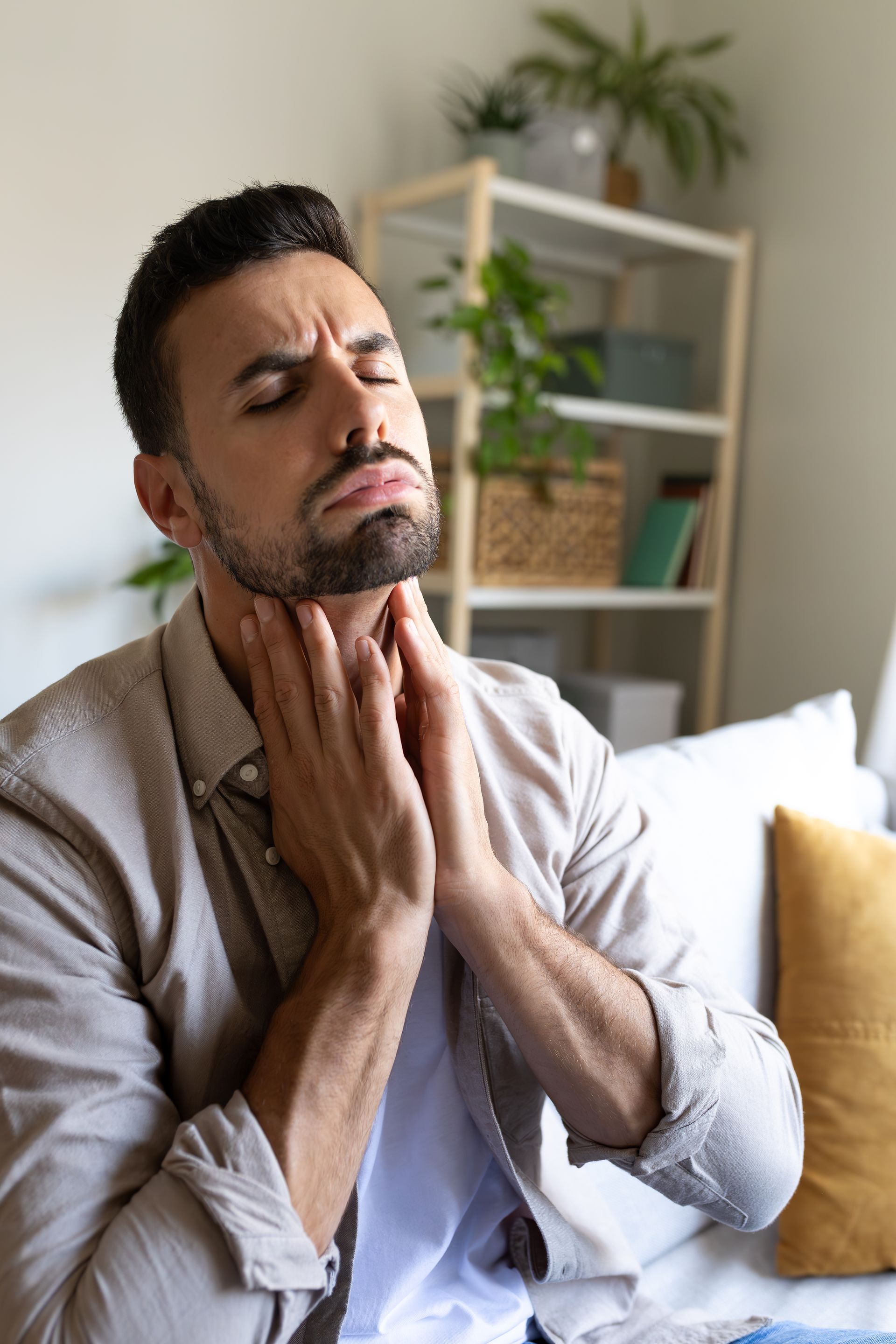 Person massaging their neck with eyes closed on a couch in a bright living room