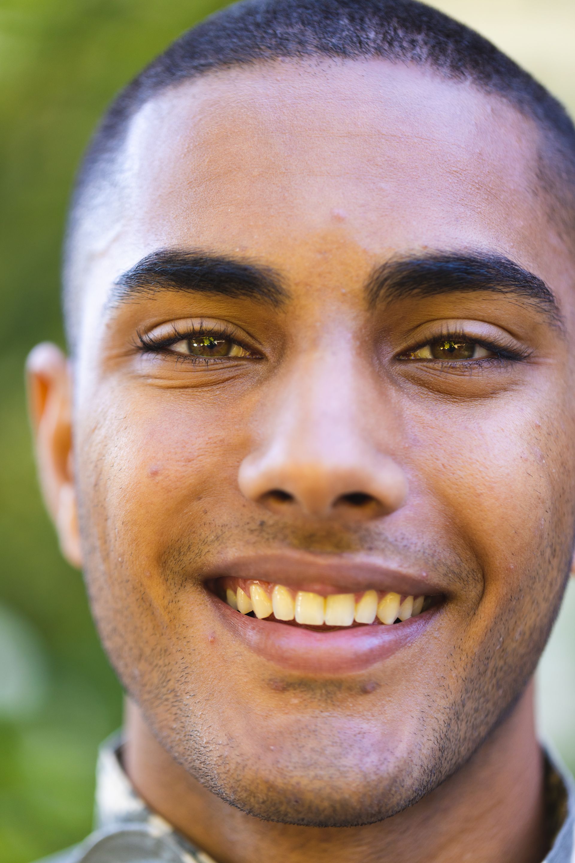 Close-up of a smiling man outdoors with a blurred green background