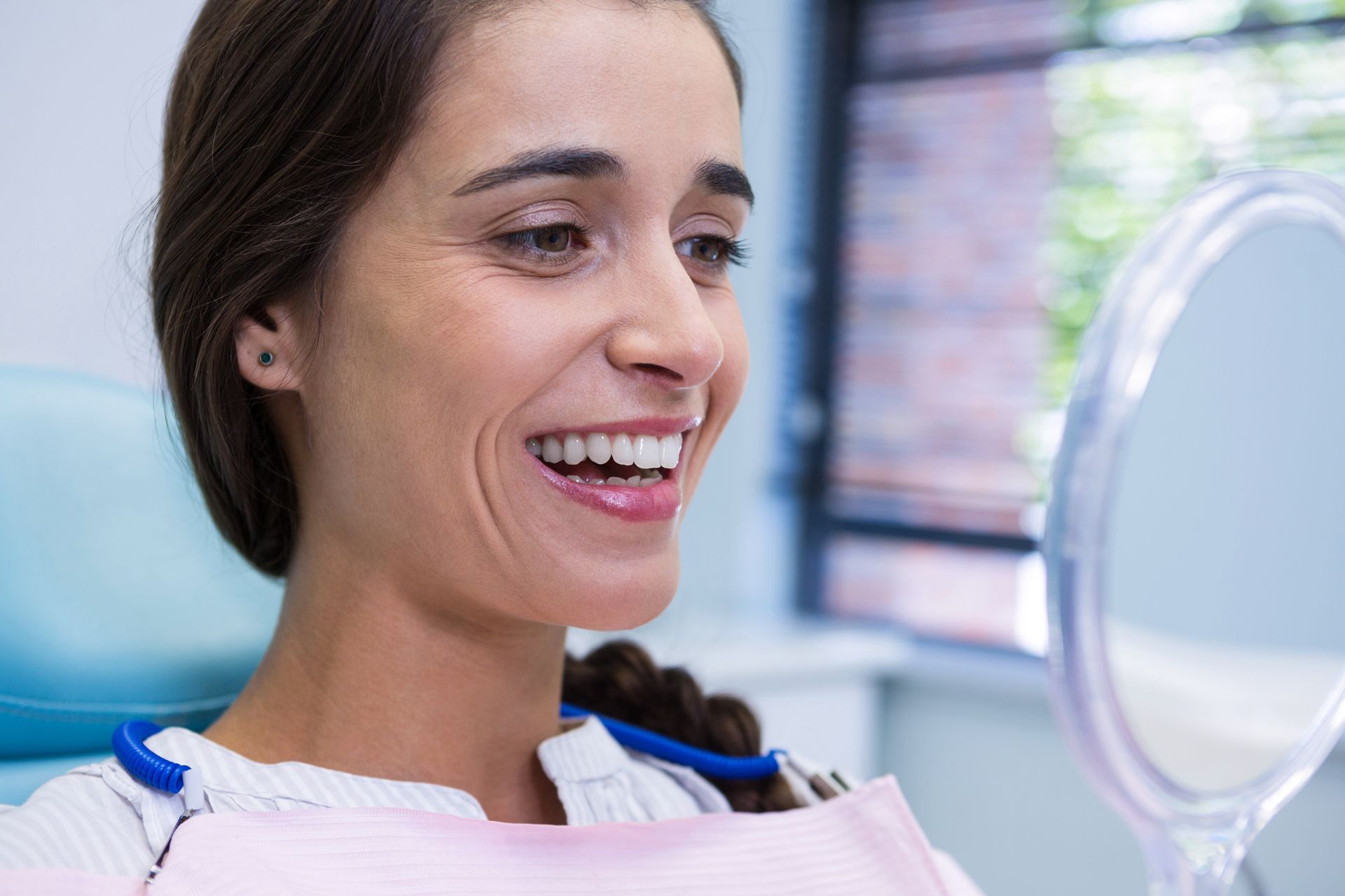 Smiling patient looking at her teeth in a dental mirror during a dental exam