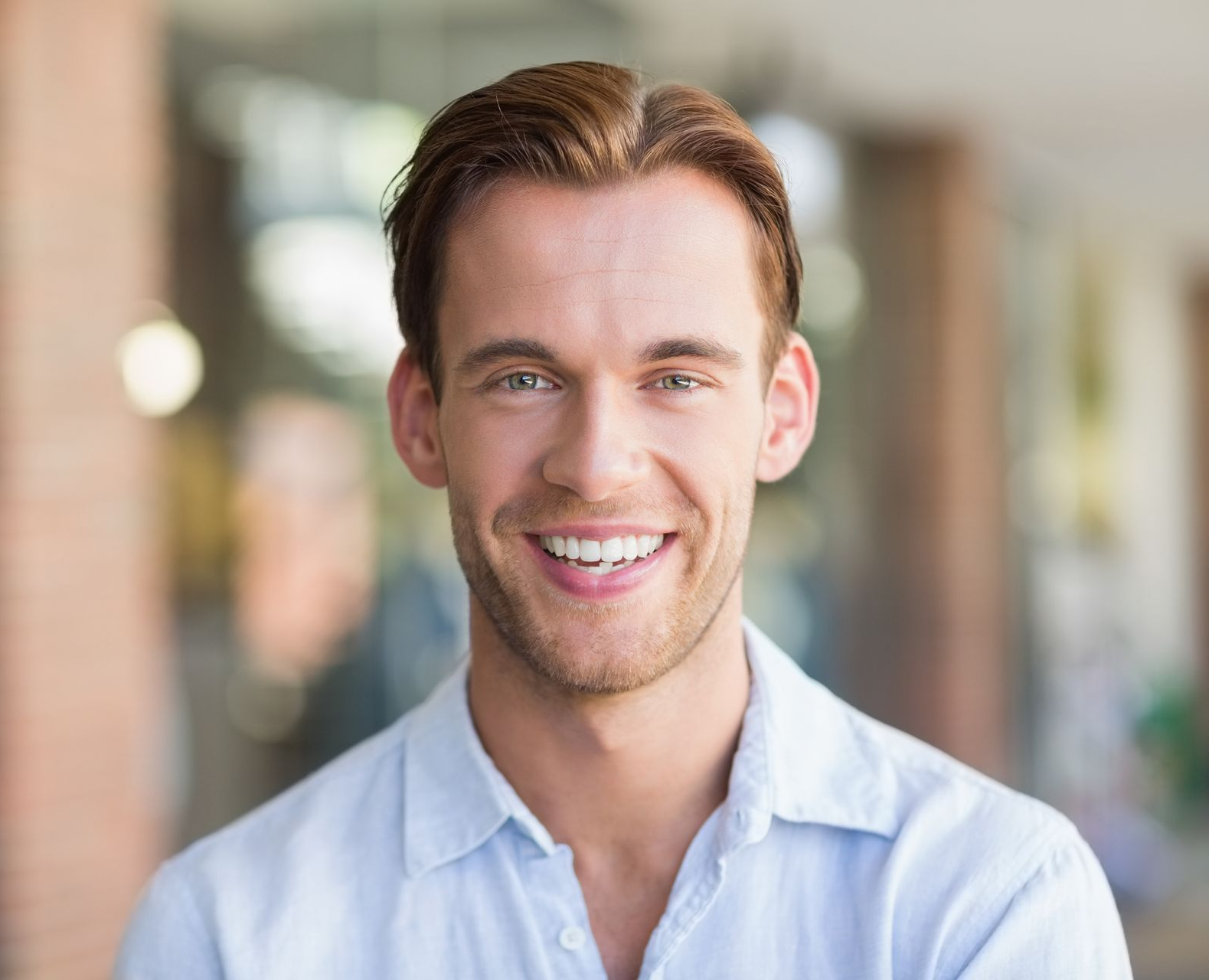 Smiling man in a light blue shirt standing outdoors with a blurred background
