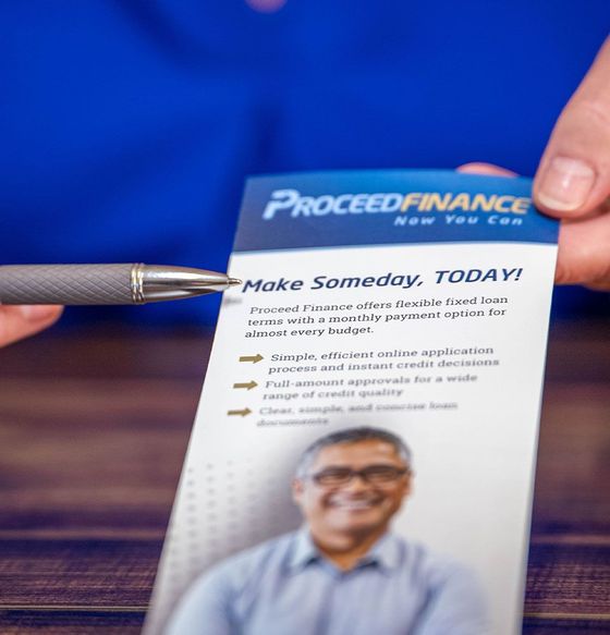 Brochure for “ProceedFinance” beside a pen on a wooden table, with blue background and a smiling man photo