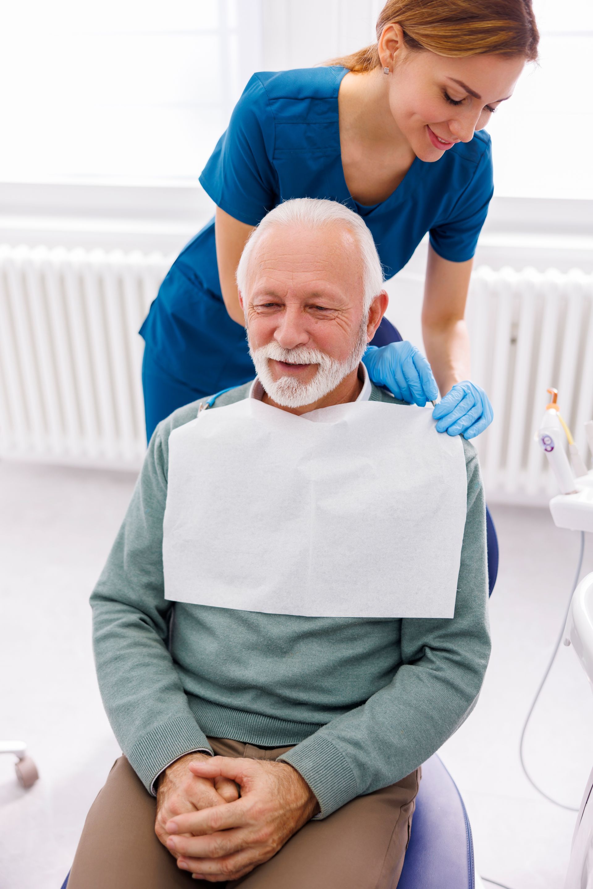 Nurse adjusting a bib on a seated patient in a bright clinical room